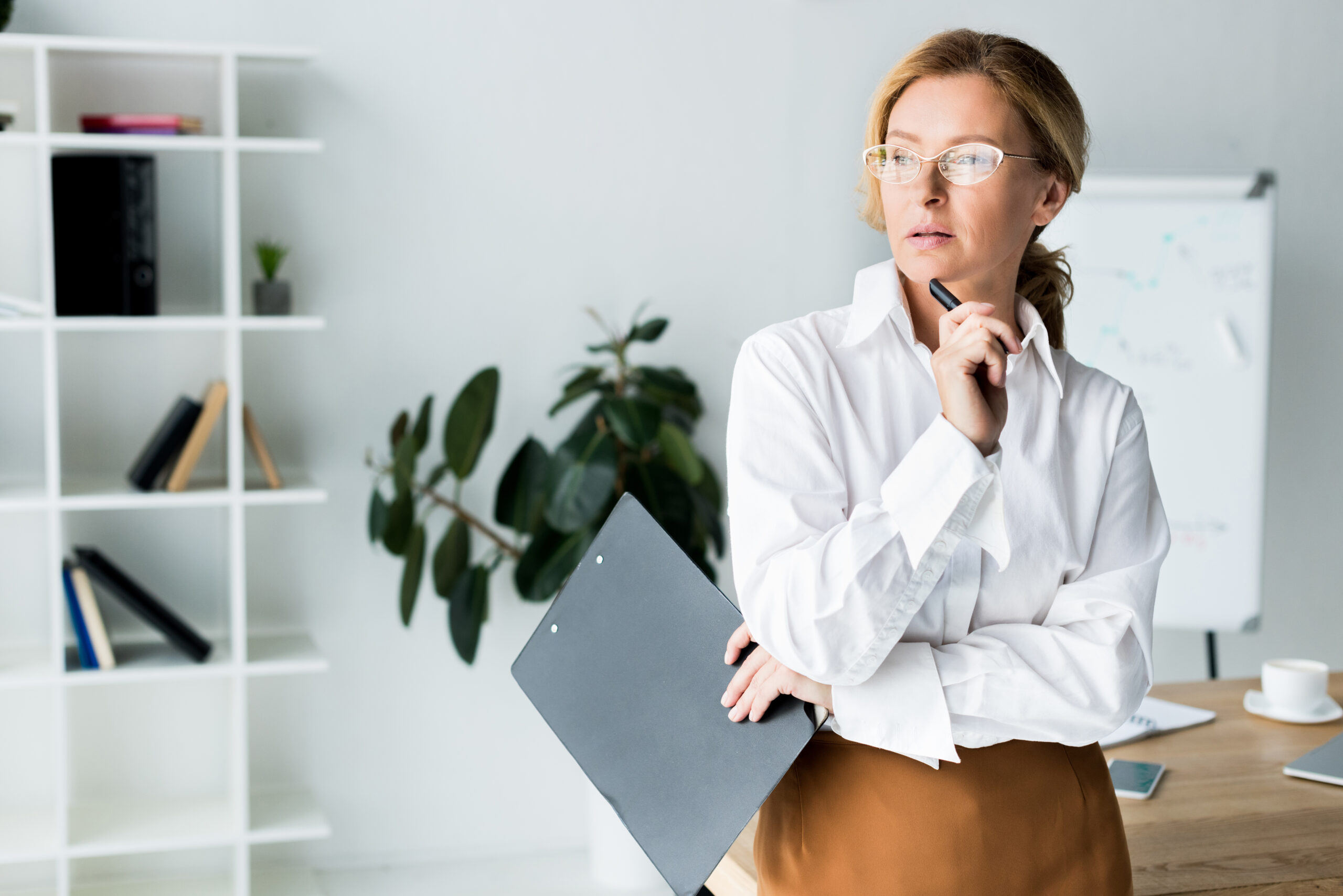 attractive businesswoman holding clipboard and looking away in office